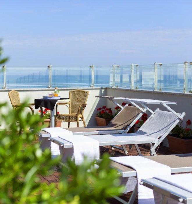 Terrazza soleggiata con lettini, fiori e vista mare, atmosfera rilassante.