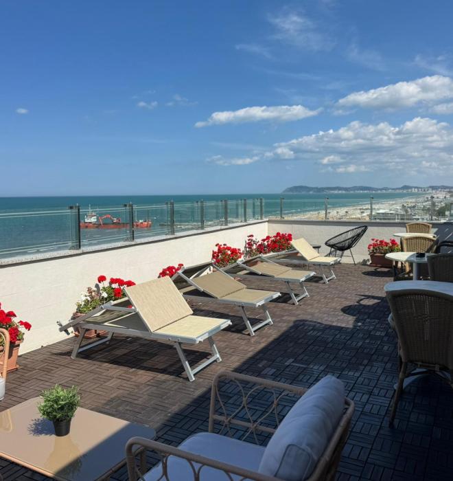 Terrazza soleggiata con vista mare, sedie a sdraio e fiori rossi.