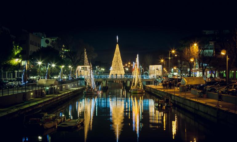 Canale illuminato con decorazioni natalizie e riflessi sull'acqua.