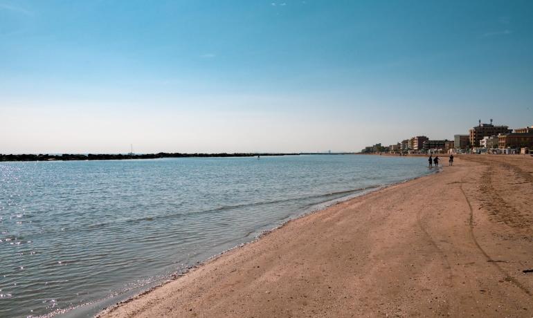 Spiaggia sabbiosa con mare calmo e cielo limpido, edifici in lontananza.