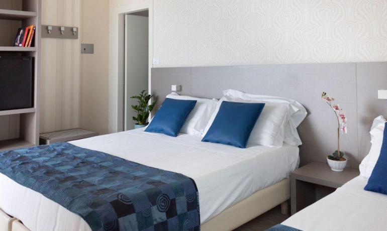 Camera moderna con letto matrimoniale, cuscini blu e decorazioni semplici.