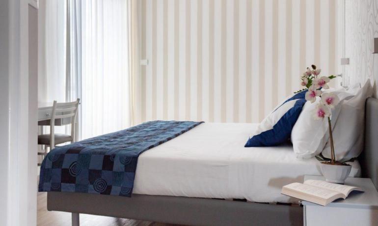Camera moderna con letto, cuscini blu e orchidea.