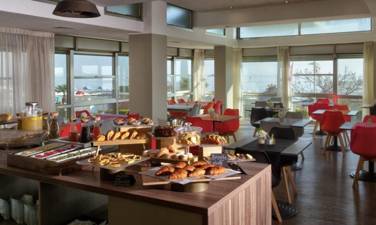 Sala colazione luminosa con buffet di dolci e vista mare.