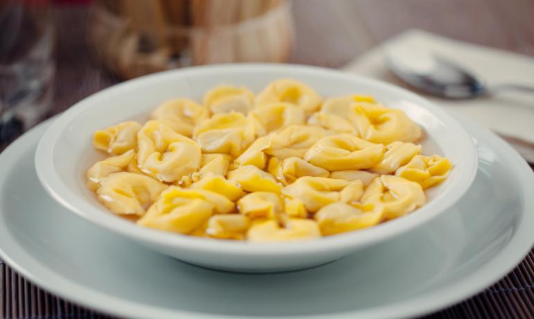 Tortellini in brodo serviti in una ciotola bianca.