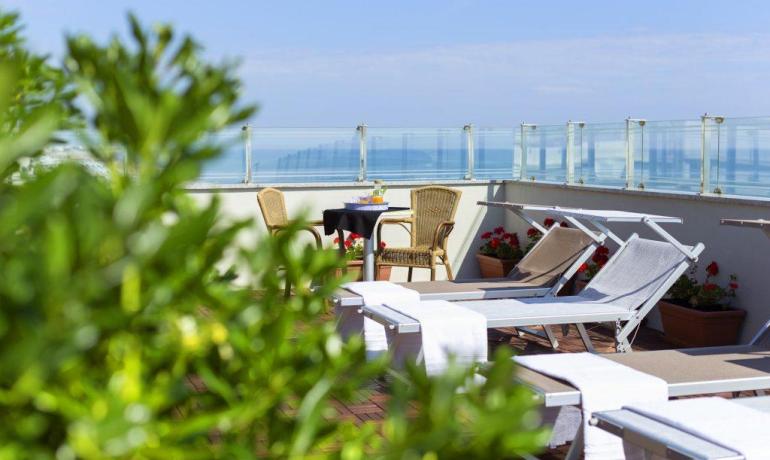 Terrazza soleggiata con lettini, fiori e vista mare, atmosfera rilassante.