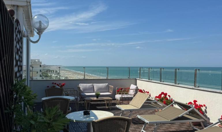 Terrazza sul mare, cielo azzurro, arredi eleganti, atmosfera rilassante e fiori colorati.