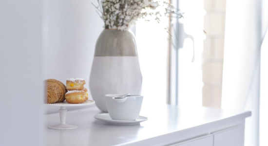 Tavolo bianco con tazza, dolci su alzata e vaso di fiori.