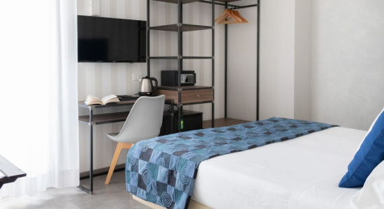 Camera moderna con letto, TV, scrivania e scaffale con bollitore e microonde.