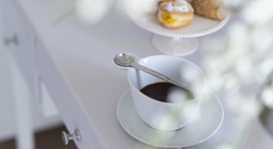 Tazza di caffè con cucchiaino, dolci su piatto, atmosfera luminosa e delicata.